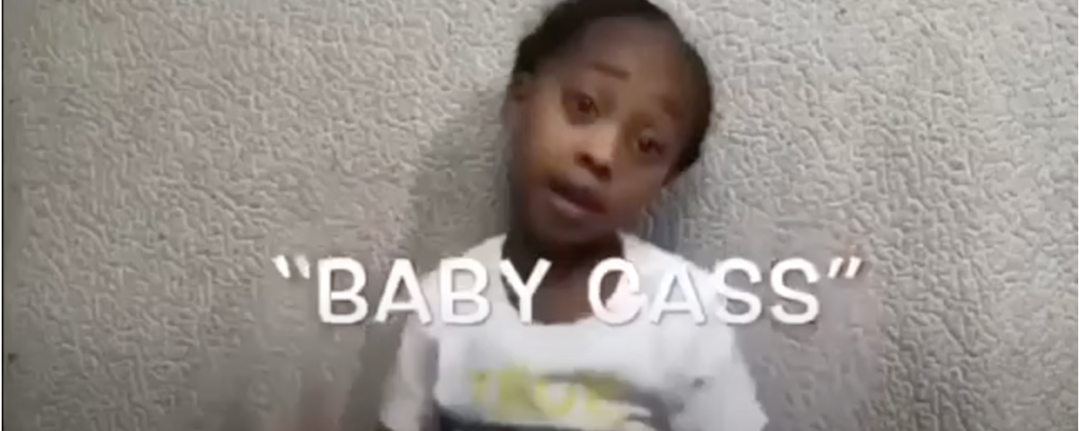 A young girl speaking, wearing a white shirt with a colorful design.